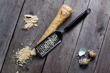 Grated horseradish root, grater and quail egg and broken shell on gray wooden background.の写真素材