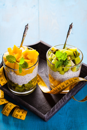 Dietetic dessert in the form of a fresh fruit salad with kiwi and peach with chia seeds and yoghurt served in a glass and lying tailor tape.の写真素材
