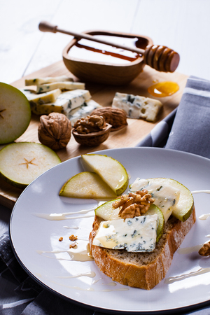 Sandwich with Blue cheese with slices of pear, nuts and honey on bamboo wooden cutting board and plate.の写真素材