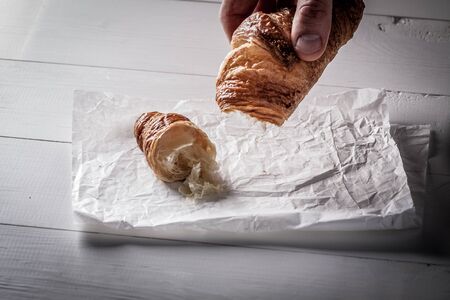 Hands tear off a piece of French pastry Croissant on white baking paper.の写真素材