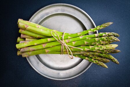 A bunch of asparagus tied with twine on a rustic silver plate.の写真素材