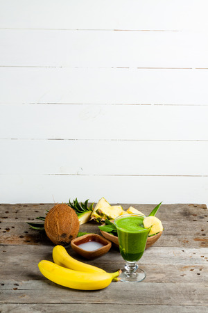 A glass of green smoothies, and the ingredients from which it was made. Smoothies with spinach, banana, coconut water, pineapple on gray wooden table.の写真素材