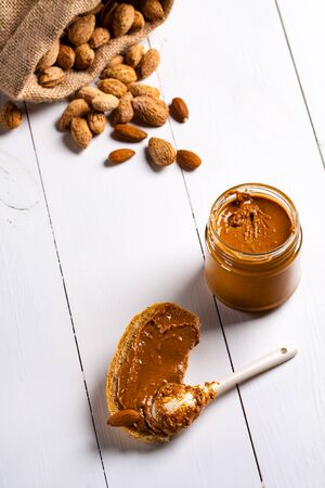 Homemade almond butter in a glass jar and sandwich smeared with a ceramic spoon.の写真素材