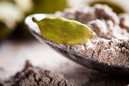 Cardamom pod lying on spoon of powdered spices.の写真素材