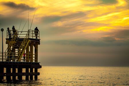 Coastal pier with silhouettes of anglers during sunset. Baltic, Poland.の写真素材