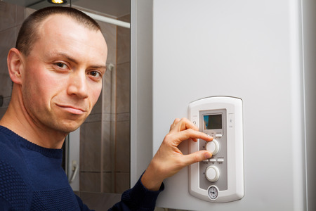 Men regulate temperature on control panel of central heating or DHW at combi boiler in restroom.の写真素材