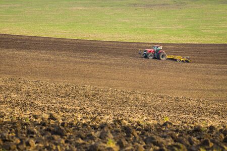Red tractor plows the field in autumn.の写真素材