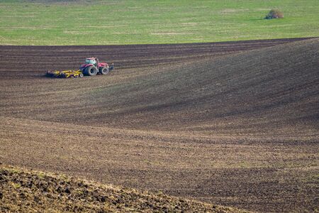 Red tractor plows the field in autumn.の写真素材