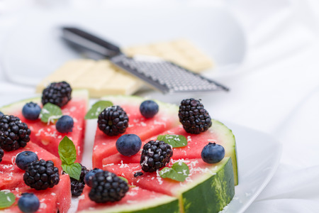 Sliced watermelon pizza with blueberries, blackberries , mint leaf and white chocolate crisps, above view.の写真素材