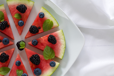 Sliced watermelon pizza with blueberries, blackberries and mint leaf, above view on white.の写真素材