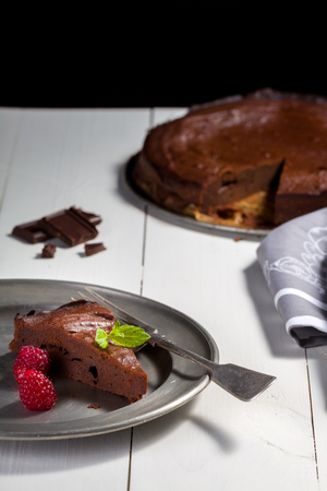 Chocolate brownie with raspberries and leaf of mint, piece lay on plate with fork, at the background is round pie.の写真素材