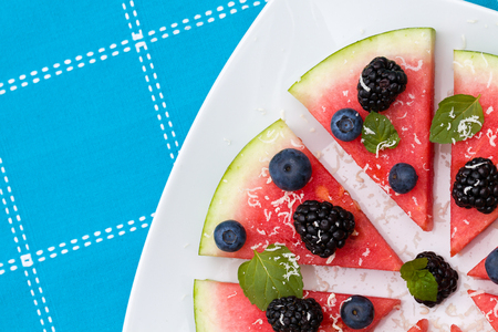 Watermelon pizza slices with fresh blueberry, blackberry, chips of white chocolate and green mint leaves.の写真素材