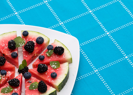 Watermelon pizza slices with fresh blueberry, blackberry, chips of white chocolate and green mint leaves.の写真素材