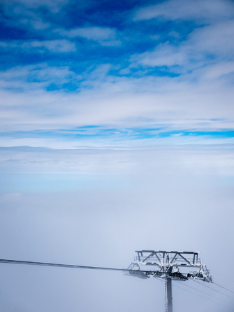 Top of ski cableway pole on clouds and blue sky.の写真素材