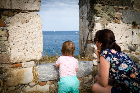 View at sea with boats through chink in the wall ancient ruins. Back view of mother with children.の写真素材
