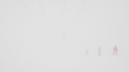 Fog on the ski resort. Ski lifts and some skiers in the fog.の写真素材