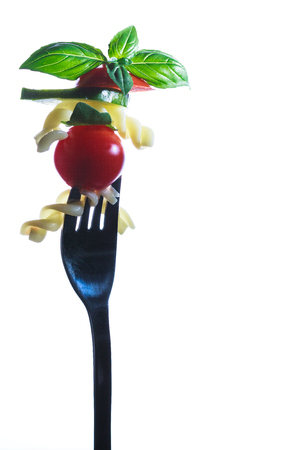 Pasta with tomato and basil leaf on a fork. Isolated on a white background.の写真素材