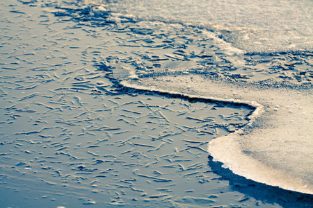 Nature background of freezing cracked water surface with reflection of sunlight.