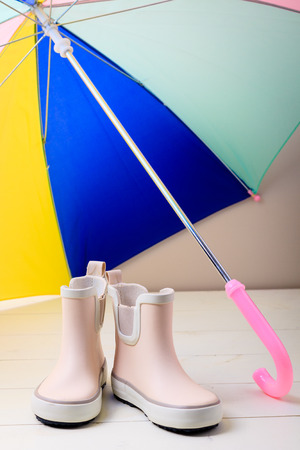 Pink little children rubber boots stand under colorful umbrella, concept of autumn or spring background.の写真素材