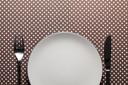 White plate with silver fork and knife on dots cardboard. Flat lay with copy space.の写真素材