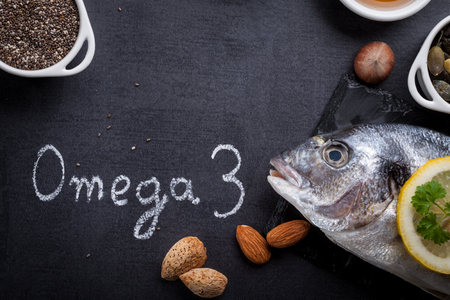 Black slate table with product rich in omega 3 and vitamin D. Written word omega 3 by white chalk.の写真素材