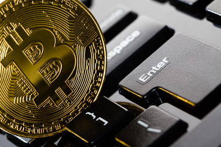 Bitcoin coin on black keyboard near enter button.の写真素材