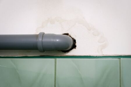 Wet stain on white wall around polypropylene gray pipe of water installation.の写真素材