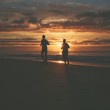 Silhouettes of couple who are running on the beach at sunrise.の写真素材