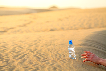 Hand try to catch the bottle of water on sand desert in hot temperature. Concept of to die of thirst.の写真素材