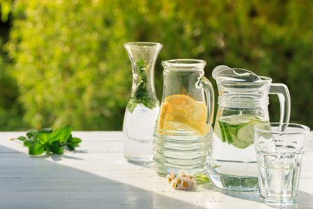Three variants of fresh homemade lemonade with lemon, cucumber and mint. Lemonade in jugs and carafe on garden. の写真素材