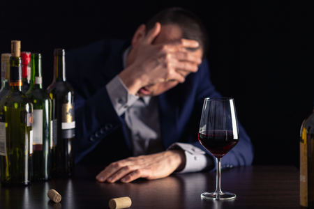 Alcohol abuse by businessman in suit. Silhouette drunk man with glass of wine on first plan.の写真素材