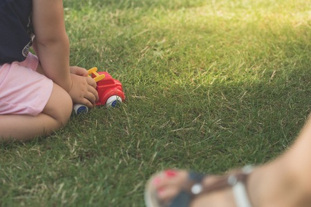 Little girl is playing red car in garden grass.の写真素材