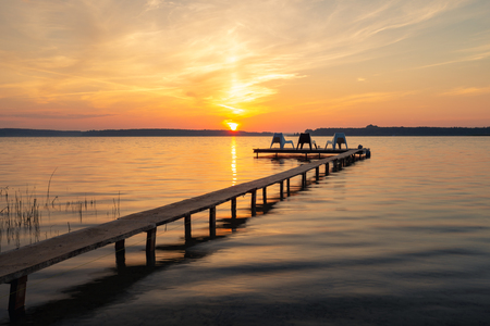 Three empty chairs on wooden jetty on lake, during sunrise.の写真素材
