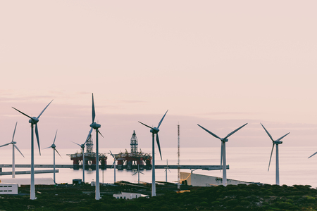 Group of windmills and solar panels for electric power production and oil rigs on coast.の写真素材