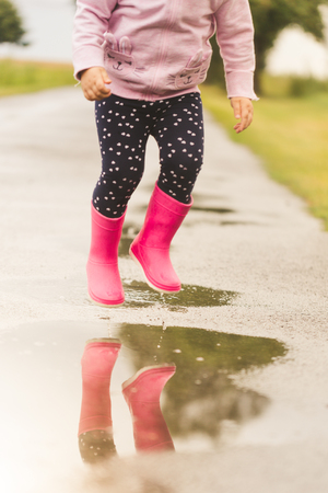 Feet of child in pink rubber boots jumping and splashing over puddle after rain.の写真素材