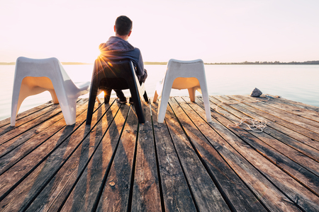 Men is relaxing and meditation on chair at footbridge on lake. Concept of waiting for summer.の写真素材
