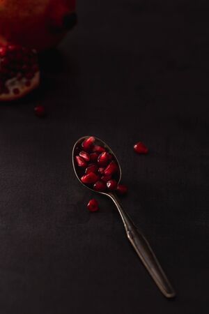 Fresh pomegranate fruits with red seeds on spoon in dark scenery.の写真素材