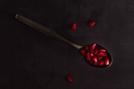 Fresh pomegranate fruits with red seeds on spoon in dark scenery.の写真素材