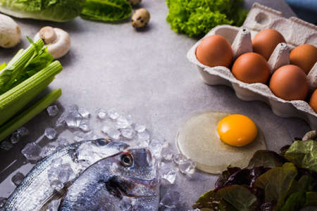 Frame of raw cooking ingredients for tasty and healthy food. Fresh dorado fish on ice, vegetables, eggs on gray concrete background top view.の写真素材