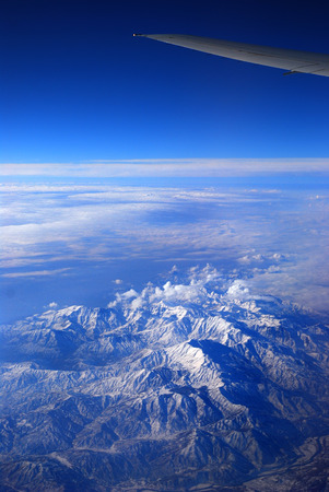 wing transport aircraft over snow-covered mountains under blue skyの写真素材