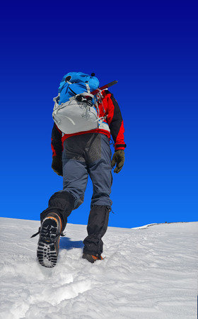 trekker with a backpack on snow, rising to the top of the mountainの写真素材