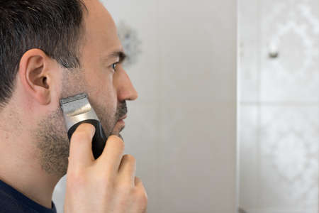 Man Trimming Beard in Bathroom with Electric Shaver on Mirrorの写真素材