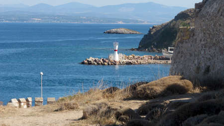 Rocky Seaside and in the Middle of the Sea a White Lighthouse の写真素材