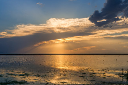 Golden sunset on a lake after storm with dark clouds and sun raysの写真素材