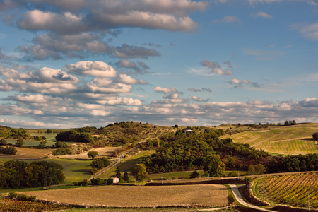 Green and yellow countryside under blue skies with white clouds and winding roadsの写真素材
