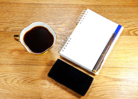cup of coffee, a phone and a notepad on a wooden backgroundの写真素材