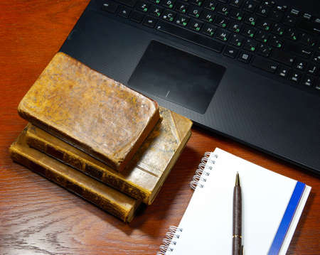 laptop, antique books and notebook on a wooden tableの写真素材