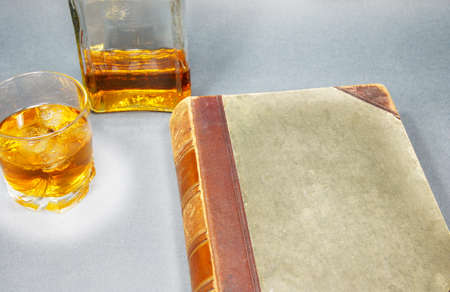 glass of whiskey, bottle and antique book on a gray backgroundの写真素材