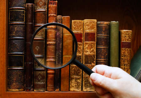 Magnifying glass in hand and the old booksの写真素材