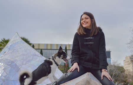 Young brunette girl smiling with a dog wearing black clothesの写真素材